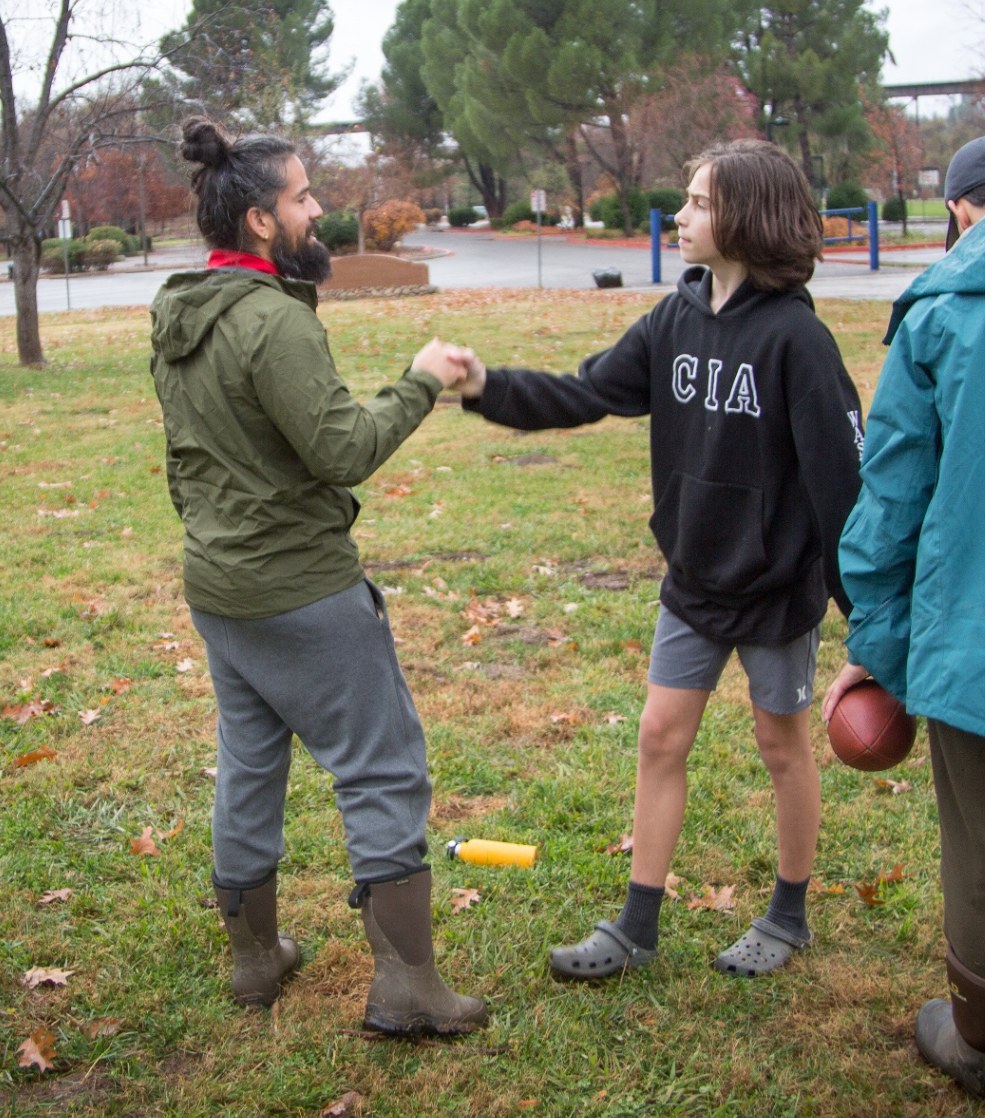Alejandro shaking hands with a young mentee in a park