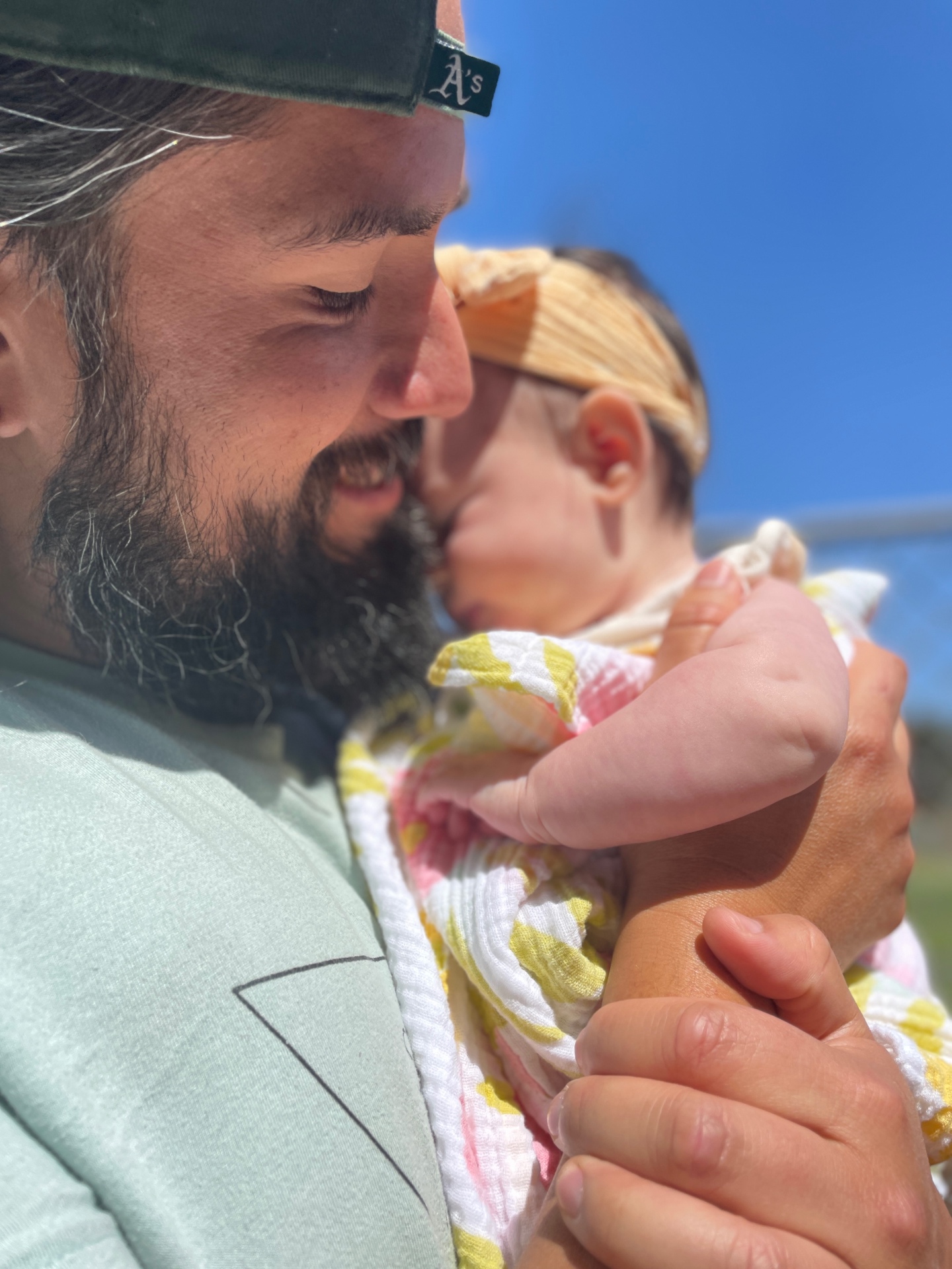 Alejandro holding his daughter close, cheek to cheek under a clear blue sky